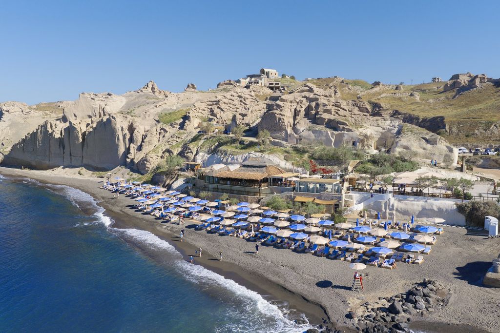 Aerial view of Royal Beach Club Santorini, a black sand beach with sun loungers below volcanic cliffs