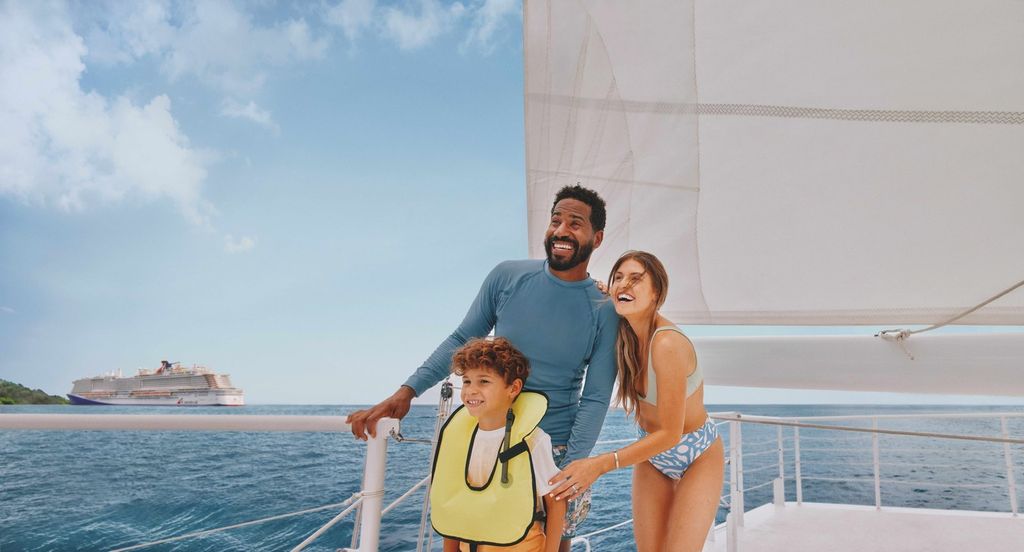 A family on a sailing boat excursion with a Carnival ship in the background