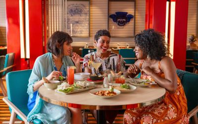 Three friends sharing dishes and cocktails at a specialty restaurant on a Carnival ship